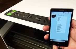 Smartphone met op achtergrond een Index brailleprinter waarvan het bedieningspaneel zichtbaar is