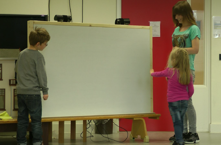 dit is een foto waar een aantal kinderen met een visuele beperking en onderzoekers samenwerken aan de geluidsmuur