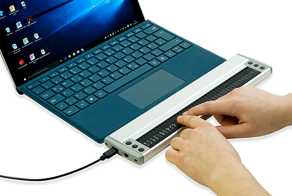 Compacte brailleleesregel die via usb-kabel verbonden is met een laptop.