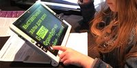 Meisje leest met schuin op het tekstblad geplaatste Snow. De tekst op het scherm is geel tegen een zwarte achtergrond. Met haar vinger bedient ze de Snow via het aanraakscherm.