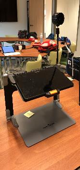 De HumanWare Prodigi Conect staat op een tafel. Het is een tablet in een houder. De table staat ongeveer 30 cm hoog
